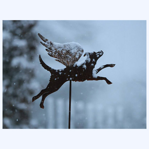 Rostiger Hundeengel als Blechfigur auf Stab im Schnee eingesteckt